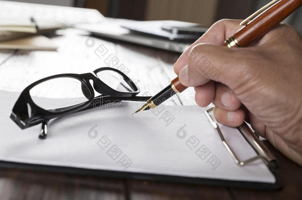手拿笔，笔记本和眼镜放在办公桌上