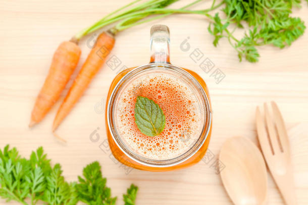 一杯胡萝卜汁，木底上有胡萝卜根。一杯美味的新鲜胡萝卜汁。胡萝卜汁和胡萝卜。