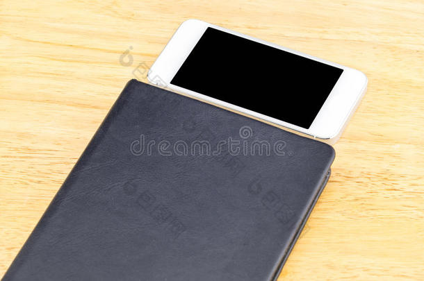 关闭黑色空白笔记本和移动在木桌上，模拟添加您的内容，裁剪路径在手机屏幕上