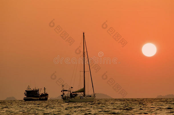日落时，游艇在海里散焦。 日落时的剪影船在海面上，背景是橙色的天空