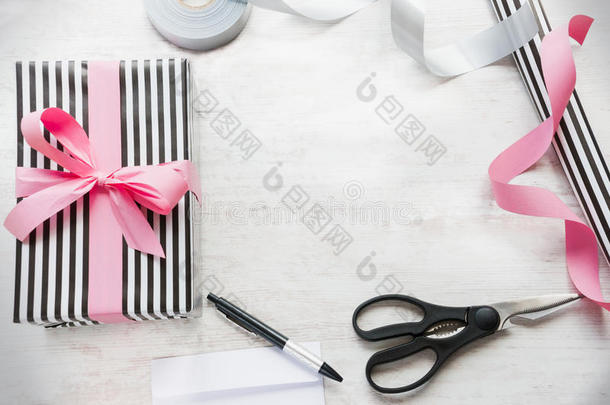 礼品盒包装在黑白条纹纸与粉红色丝带和包装材料的白色木材旧背景。