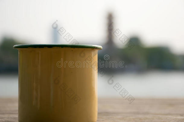 把黄色的杯子放在河边的一张木桌上。 背景