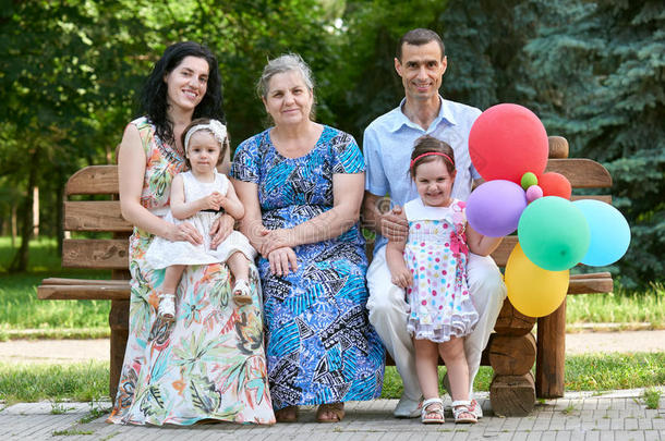 大家庭<strong>坐</strong>在城市公园的木凳上，夏天，孩子，父母和祖母，五个人带着<strong>气球</strong>