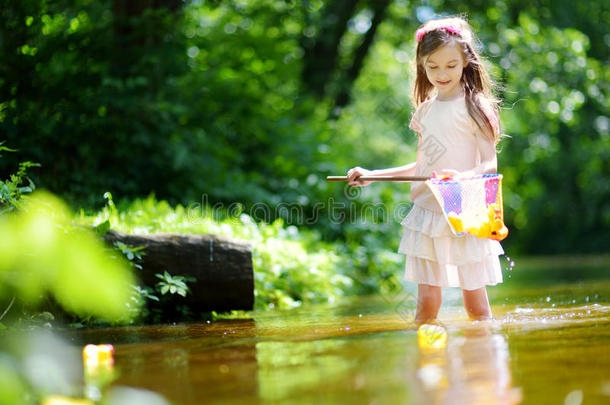 可爱的小女孩在河里玩，用她的独家新闻捕捉橡胶鸭子