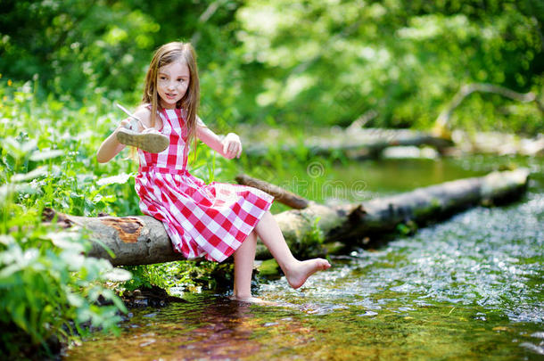 阳光明媚的夏天，可爱的<strong>小</strong>女孩坐在<strong>河边</strong>的一根木头上