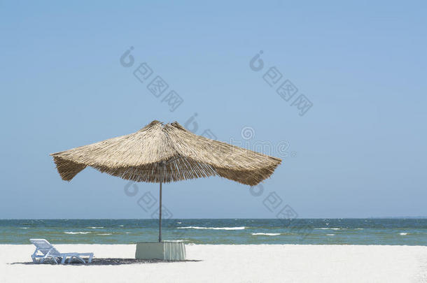 海滩草伞从阳光下的海滩上带着太阳床，在<strong>大海</strong>和蓝天的<strong>背景</strong>下，