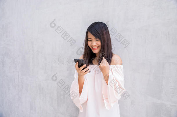 漂亮的亚洲女人在混凝土墙上用手机