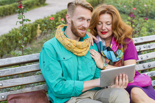 一对夫妇<strong>坐在公园里</strong>，男人和女人看着平板电脑