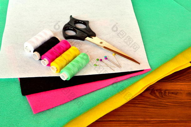 绿色，粉红色，黄色，白色和黑色毡床单。 木桌上的剪刀、线和别针