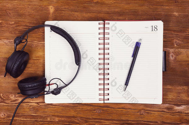 空白记事本，木制桌子背景上有钢笔和耳机。 记事本，钢笔和耳机。 上面的风景。 看起来
