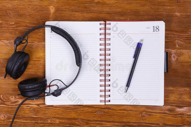 空白记事本与钢笔和耳机在老式木桌背景。 记事本，铅笔和耳机。 上面的风景。