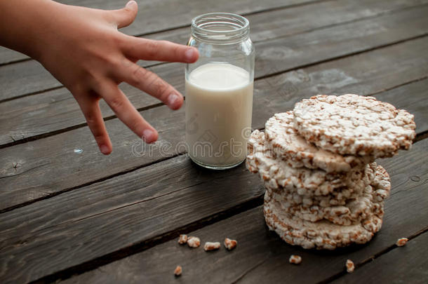 孩子的手把牛奶带回家。 美味的脆饼在木制背景桌子上
