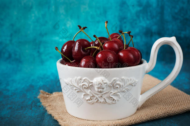 新鲜樱桃放在白色的碗里，一个大杯子。 新鲜水果，水果沙拉。 蓝色背景。 乡村风格