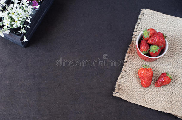 新鲜草莓在迷你金属桶上的黄麻。 白色和紫色的花在装饰木箱里。 黑色背景。