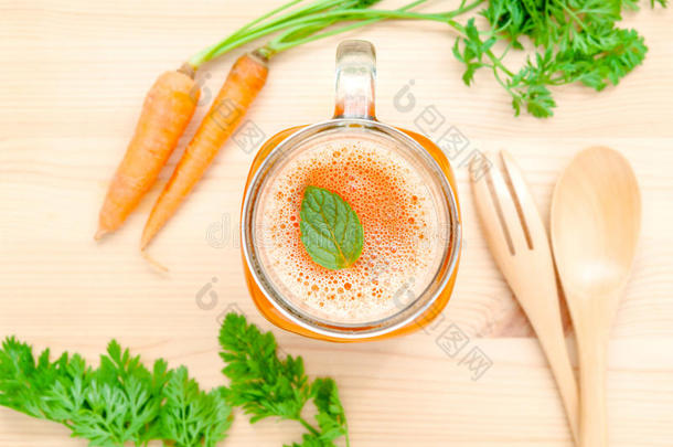 一杯胡萝卜汁，木底上有胡萝卜根。一杯美味的新鲜胡萝卜汁。胡萝卜汁和胡萝卜。