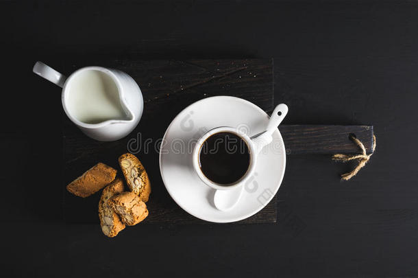一杯热的浓缩咖啡，牛奶和饼干在黑色背景的深色乡村木板上