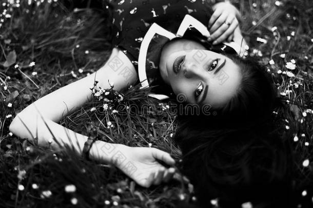 黑白相间的年轻女人的肖像，躺在草地上，开着小花。 上面的风景
