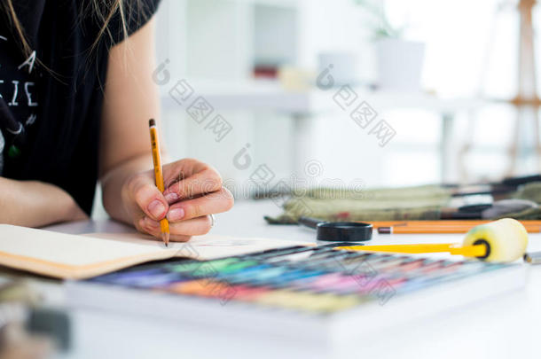 用铅笔在素描簿上画草图的女画家的特写角度视图。 艺术家在艺术工作室写生