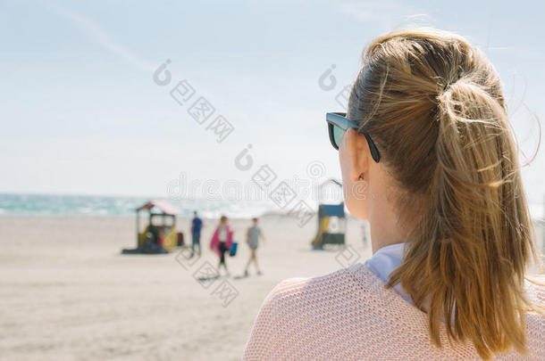 戴太阳镜的金发女孩看着大海，在靠近TH的风天