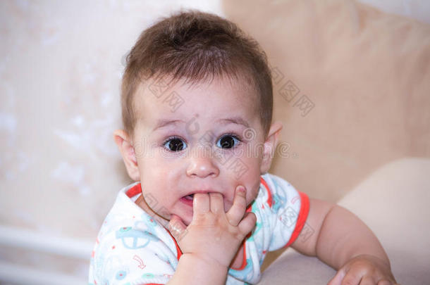 小男孩在嘴里玩手指和快乐的面部表情。 爬行微笑的肖像。 蹒跚学步的婴儿玩耍。 纽伯