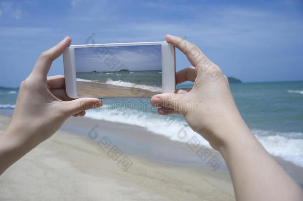 特写女人的手拿着智能<strong>手机</strong>，<strong>手机</strong>，智能<strong>手机</strong>在模糊美丽的蓝海上拍一张大海的照片