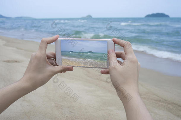 特写女人的手拿着智能手机，手机，智能手机在模糊美丽的蓝海上拍一张大海的照片