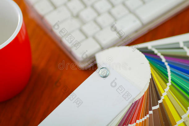 特写大调色板彩色展开在白色电脑键盘和红色咖啡杯前坐在木桌上