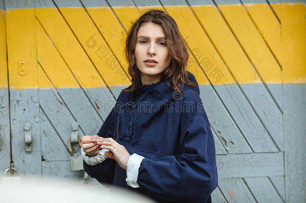 在阴天，时尚漂亮的女人在仓库门口摆姿势的时尚肖像。 穿着时髦的城市服装，长夹克。