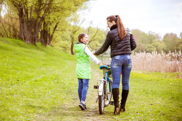 女儿和母亲骑着自行车沿着湖边散步，交谈。 家庭<strong>价值观</strong>教育