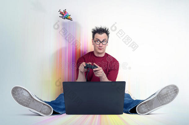 带操纵杆的有趣的人坐在<strong>笔记本</strong>电脑前面的五彩地板上。 <strong>玩家</strong>玩。