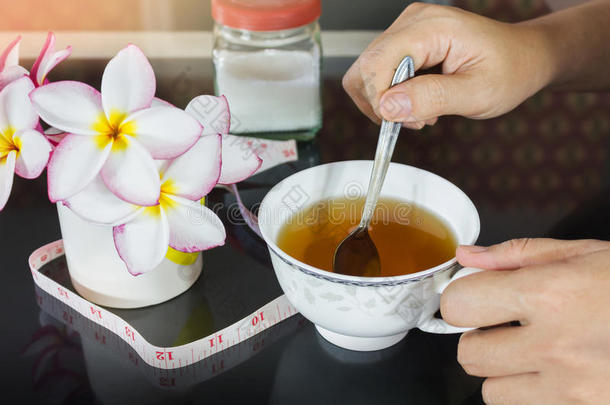 手拿一杯茶和背景的磁带测量和糖，饮食或减肥茶，一杯泻药茶和女孩或妇女h