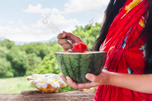 专注于勺子上的西瓜和女人手拿西瓜，女人穿着轻松的夏装在阳光下吃西瓜