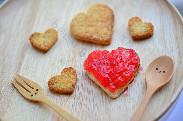 面包切割和红色草莓果酱的形状的心脏和木制勺子与微笑隔离在白色背景(概念