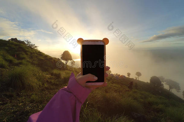 一只手在山顶用智能手机拍照。 日出的灯光色调。