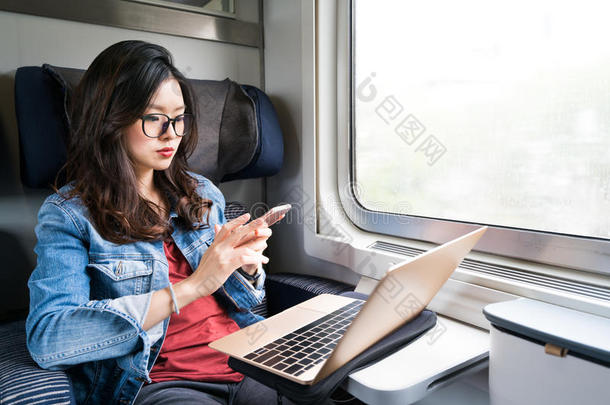 可爱的亚洲女人在火车上使用智能手机和笔记本电脑，在窗户上复制空间，<strong>商务旅行</strong>或技术概念