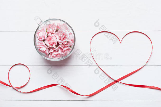 玻璃杯充满粉红色玫瑰与红色心形丝带在白色木制桌面景观