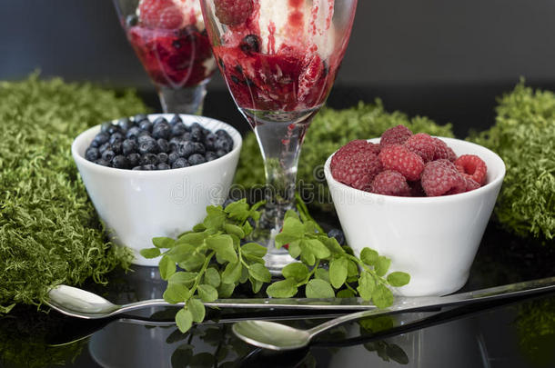 白色碗里的水果和银勺子，玻璃里的冰淇淋。 加<strong>覆盆子</strong>、蓝莓和<strong>覆盆子</strong>糖浆的冰淇淋