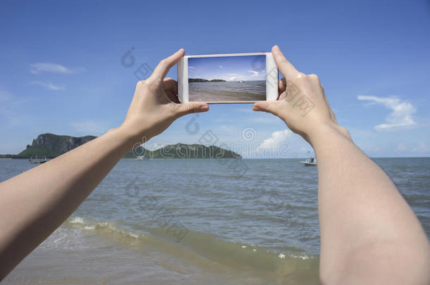 靠近女人的手，拿着智能手机，手机，智能手机在模糊美丽的蓝海和渔船上