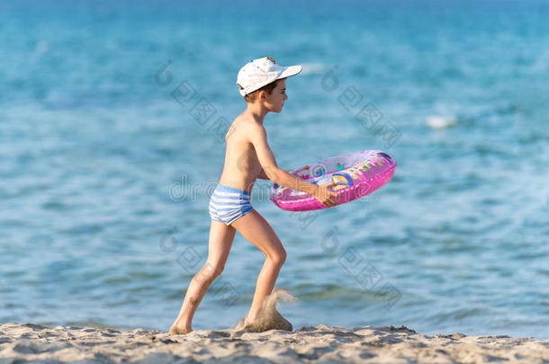 漂亮的男孩带着救生圈在沙滩上奔跑