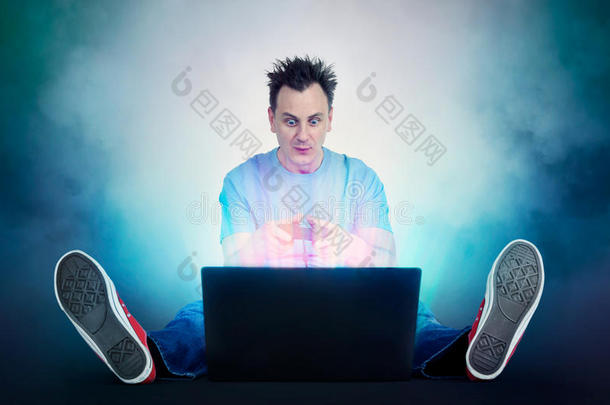 带操纵杆的滑稽男人坐在<strong>笔记本</strong>电脑前的地板上。 <strong>玩家</strong>玩。