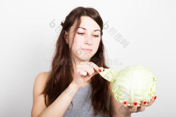 美丽的年轻女人吃蔬菜。 拿着卷心菜，她盯着卷心菜的头。 健康的食物-健康