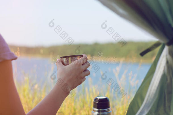 女孩徒步旅行者在帐篷里拿着一杯温<strong>暖</strong>的<strong>茶</strong>。 背景中的山脉和湖泊。