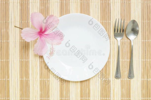 特写白色陶瓷菜与不锈钢叉子和勺子与粉红色的花在木<strong>垫</strong>纹理<strong>背景</strong>的餐<strong>桌</strong>在顶部