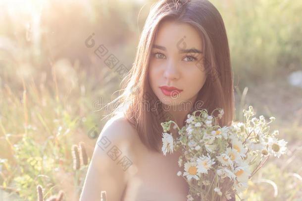 美丽的<strong>甜美女</strong>孩，丰满的嘴唇坐在田野里，带着一束雏菊，在日落的时候，有着奥诺真尼米的肩膀