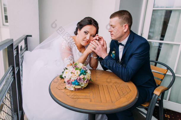 华丽的新娘和优雅的新郎坐在<strong>阳台</strong>的<strong>桌子</strong>上，有甜蜜的时刻。 新婚蜜月的概念