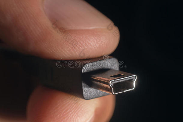 手拿黑色迷你USB电缆。 男人的手拿着一个USB迷你连接器。