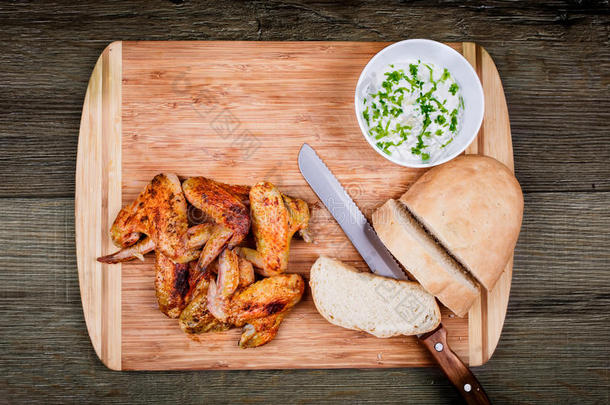 美味的<strong>烤鸡</strong>翅与大蒜酱，刀和面包在一个切割板上的木制乡村背景顶部