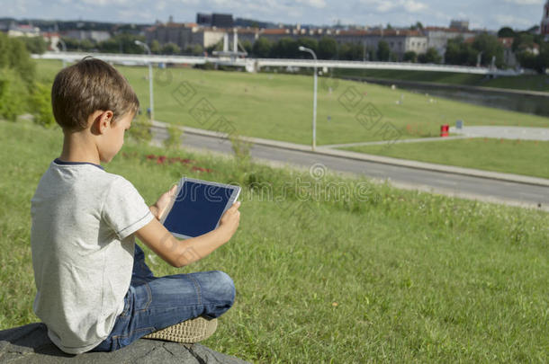 儿童与平板电脑户外。 草地上的男孩拿着电脑。 后视图。 科技人教育理念