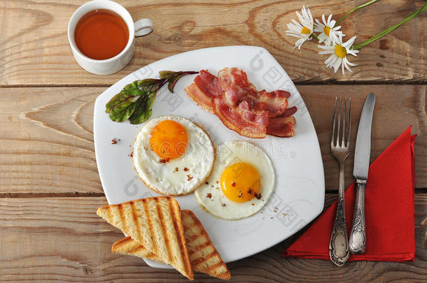 早餐-煎鸡蛋，吐司，培根，茶和洋甘菊在木制背景