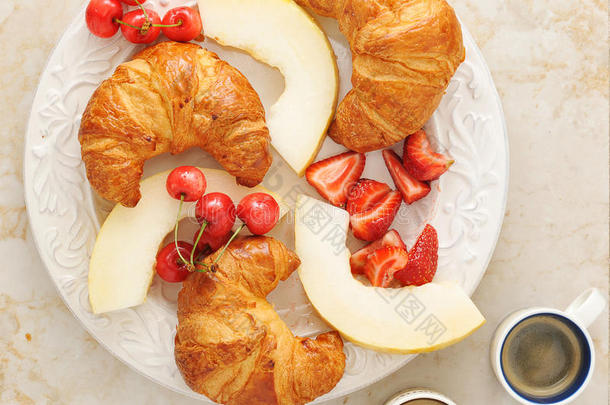 早餐包括咖啡、牛角面包和水果-甜瓜、草莓、樱桃。